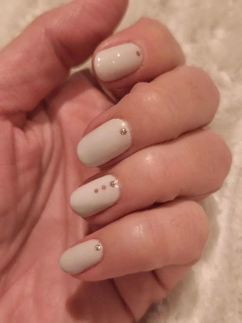 Uñas ovaladas en blanco roto con pequeñas piedras doradas, hechas en Dream Nails