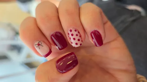 Uñas en granate con lunares y un lazo pintado a mano